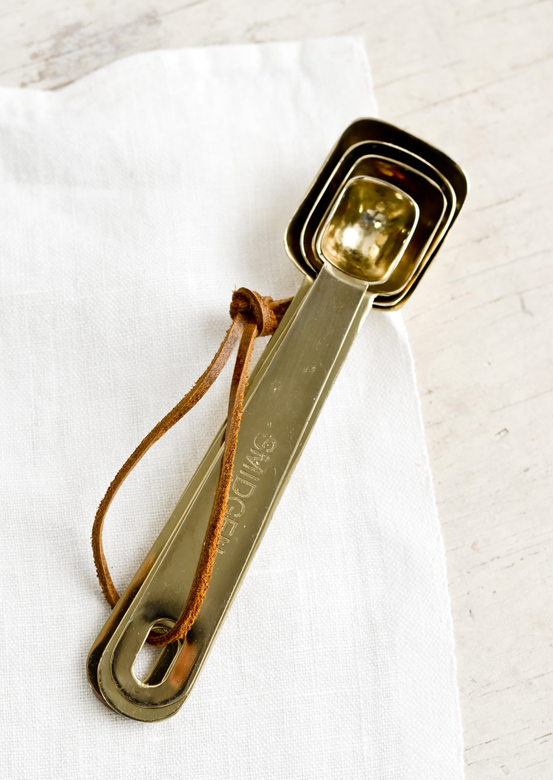 A set of four golden measuring spoons with brown leather tie.