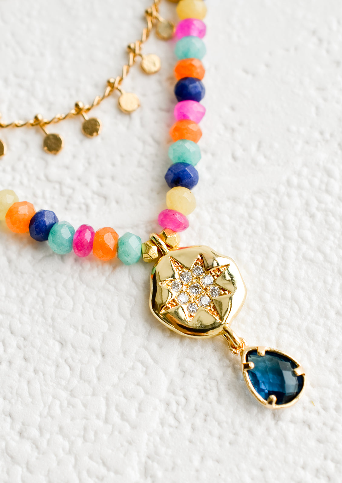 A gold charm with CZ detailing on a beaded necklace.