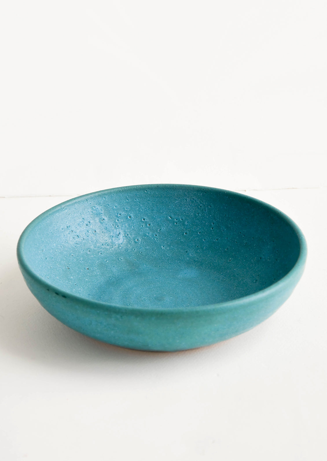 Handmade ceramic bowl in wide, shallow shape and rustic turquoise glaze