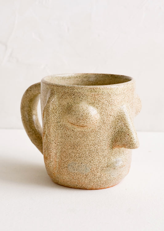 A clay mug in speckled sand color in face shape.
