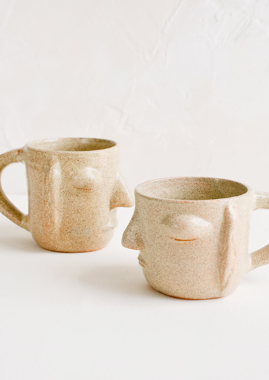 Two face shaped mugs in speckled sandy clay.