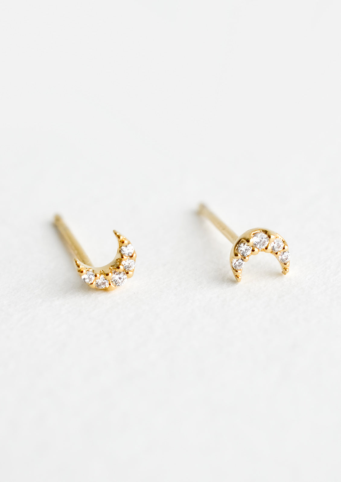 A pair of very tiny gold stud earrings in the shape of crescent moons, covered in clear crystals.