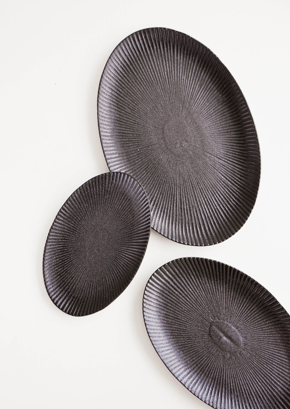 Oval-shaped, black ceramic trays with radiating lines pattern in a mix of incremental sizes
