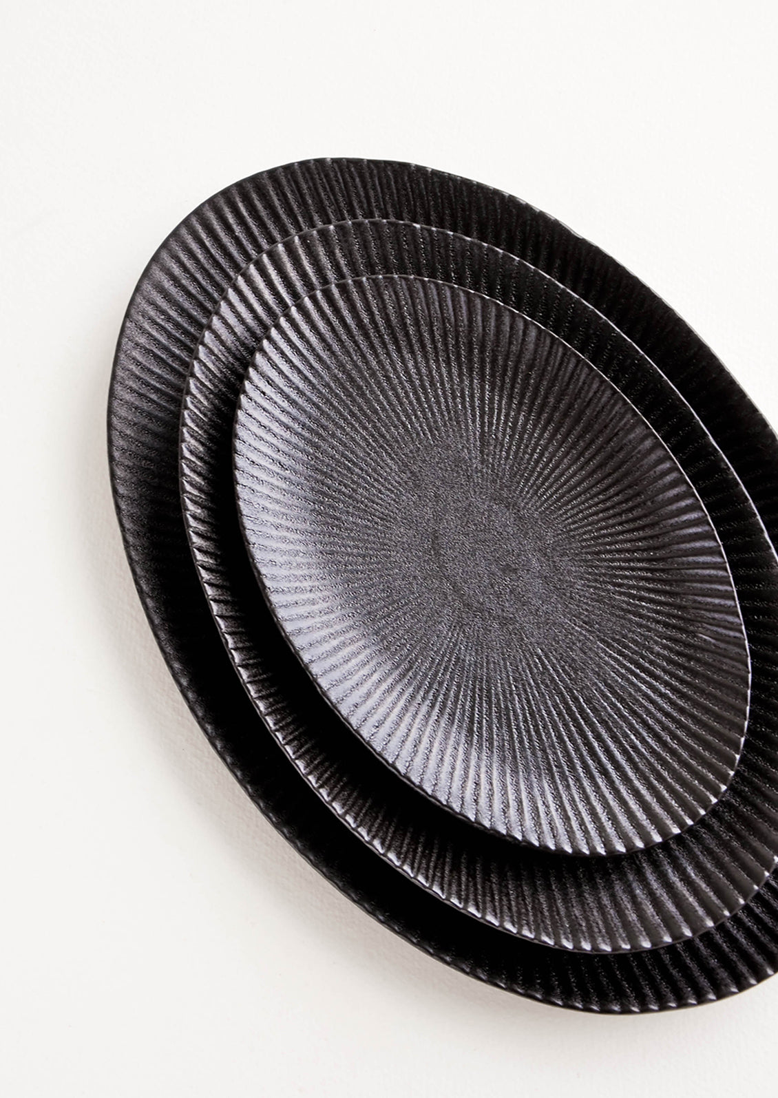 Oval-shaped, black ceramic trays with radiating lines pattern stacked in incremental sizes