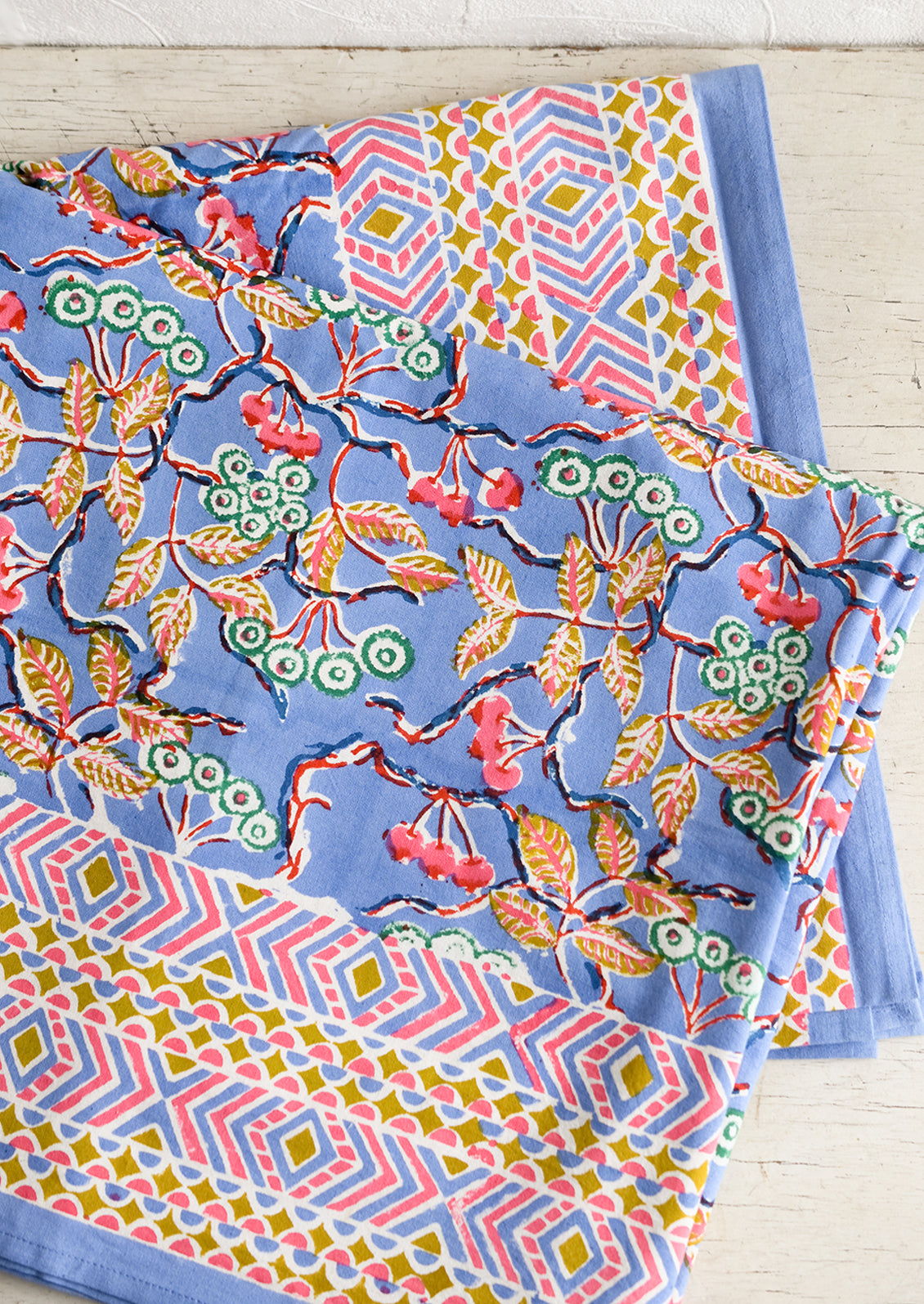 A block printed table cloth in yellow, blue and pink floral print with geometric border.