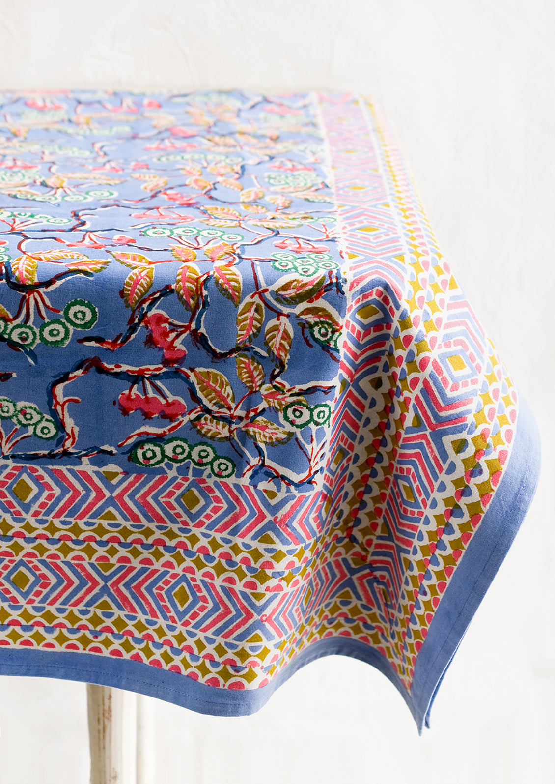 A block printed table cloth in yellow, blue and pink floral print with geometric border.