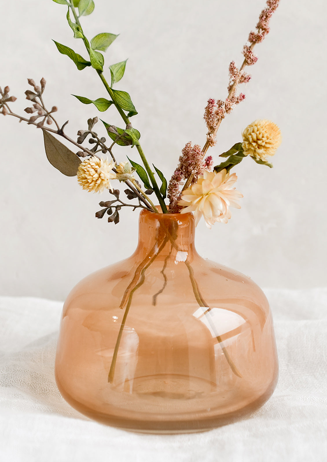 A peach glass bud vase with dried flowers.