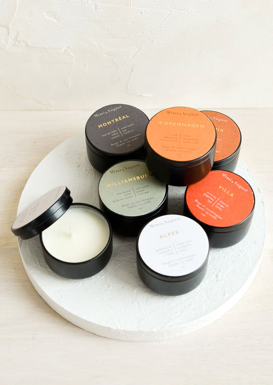 Small soy candles in assorted scents, packaged in black metal tins.