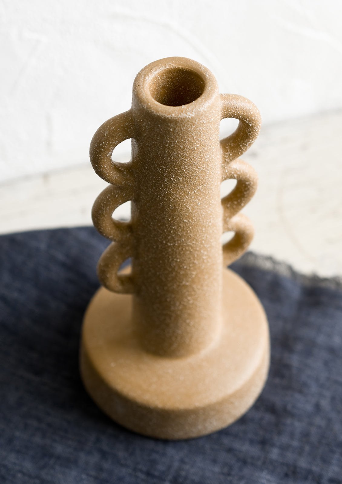 A textured sand colored taper holder with decorative loop shape.