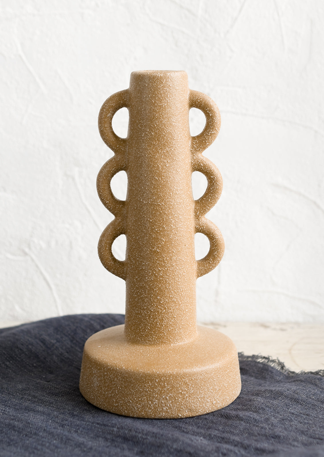 A textured sand colored taper holder with decorative loop shape.