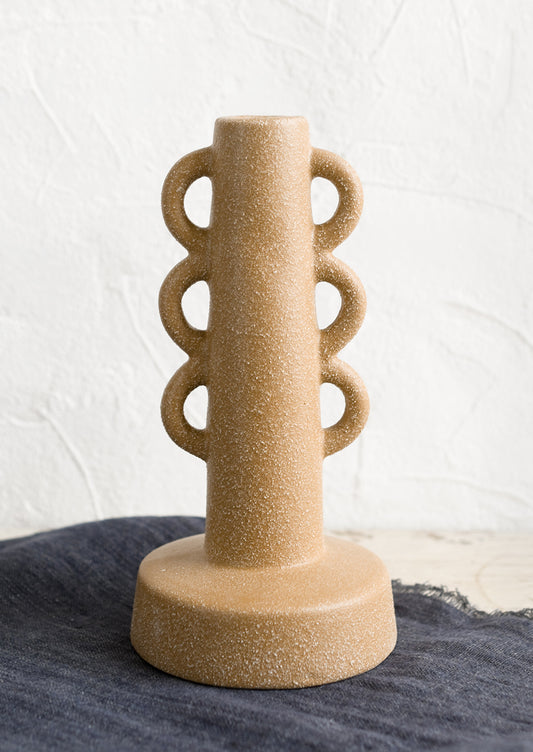 A textured sand colored taper holder with decorative loop shape.