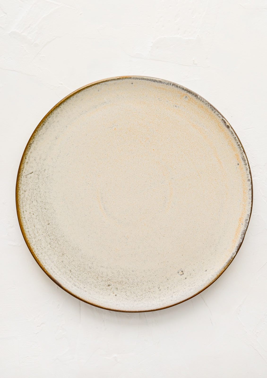 A round ceramic plate in matte cream glaze with subtle speckled texture.