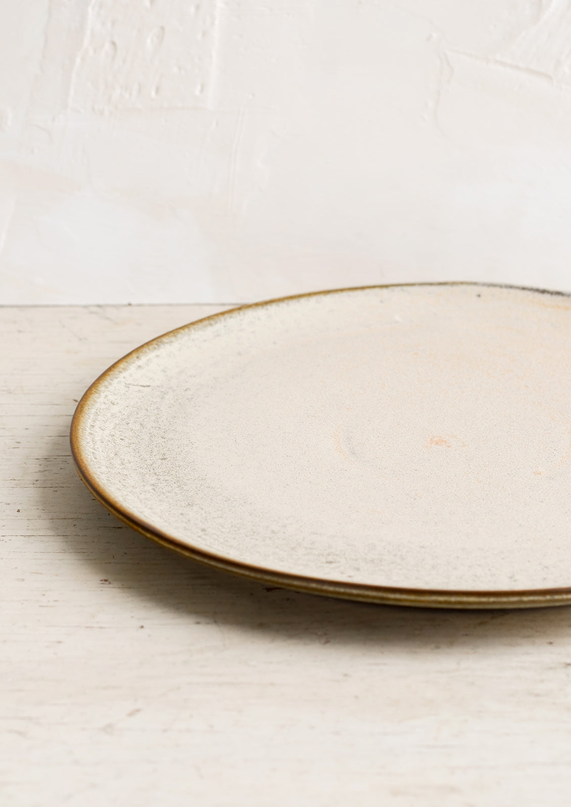 A round ceramic plate in matte cream glaze with subtle speckled texture.