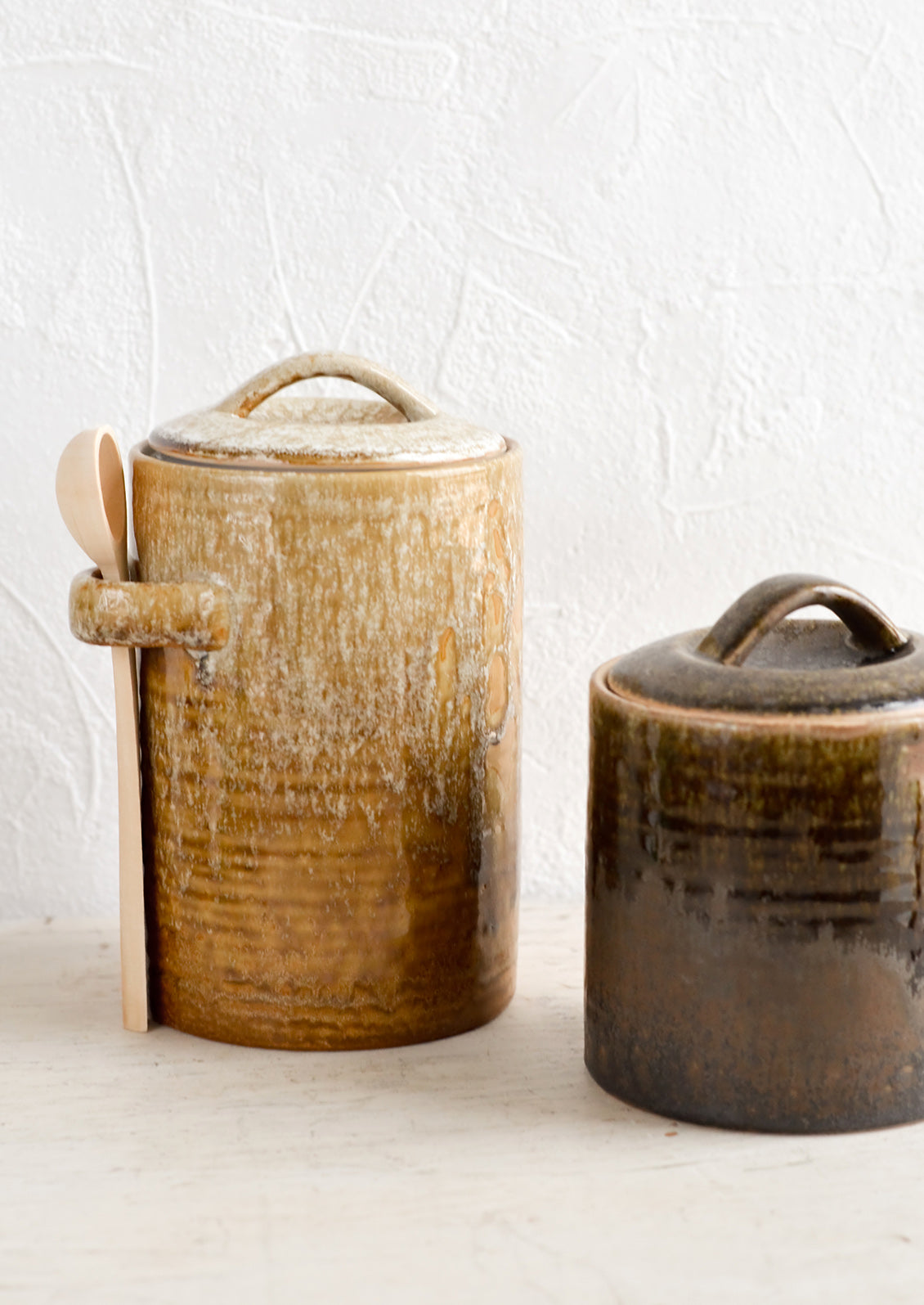 Two ceramic storage jars in short and tall sizes, glazed in light and dark brown glazes.
