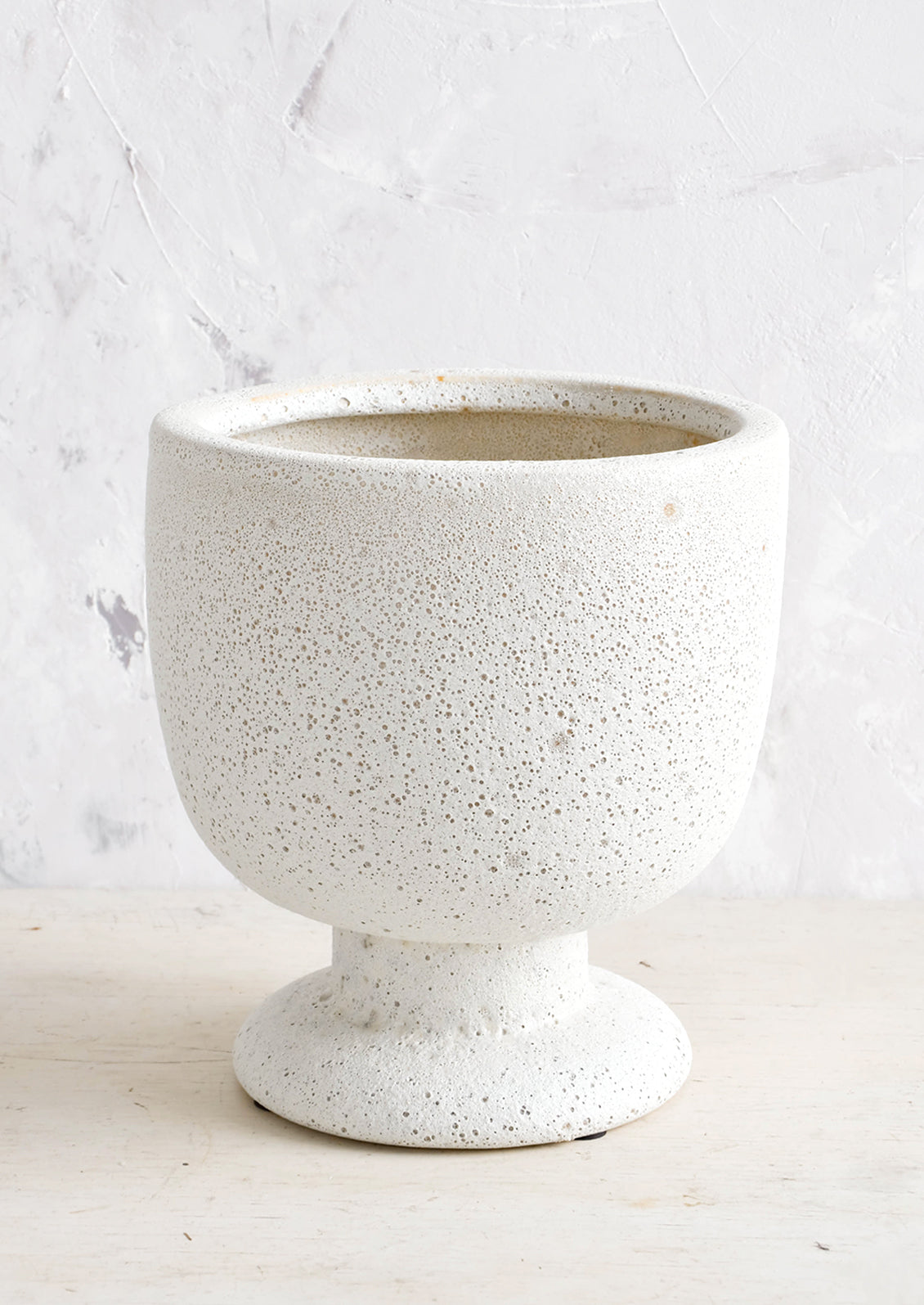 A planter in matte light grey textured glaze and footed urn shape.