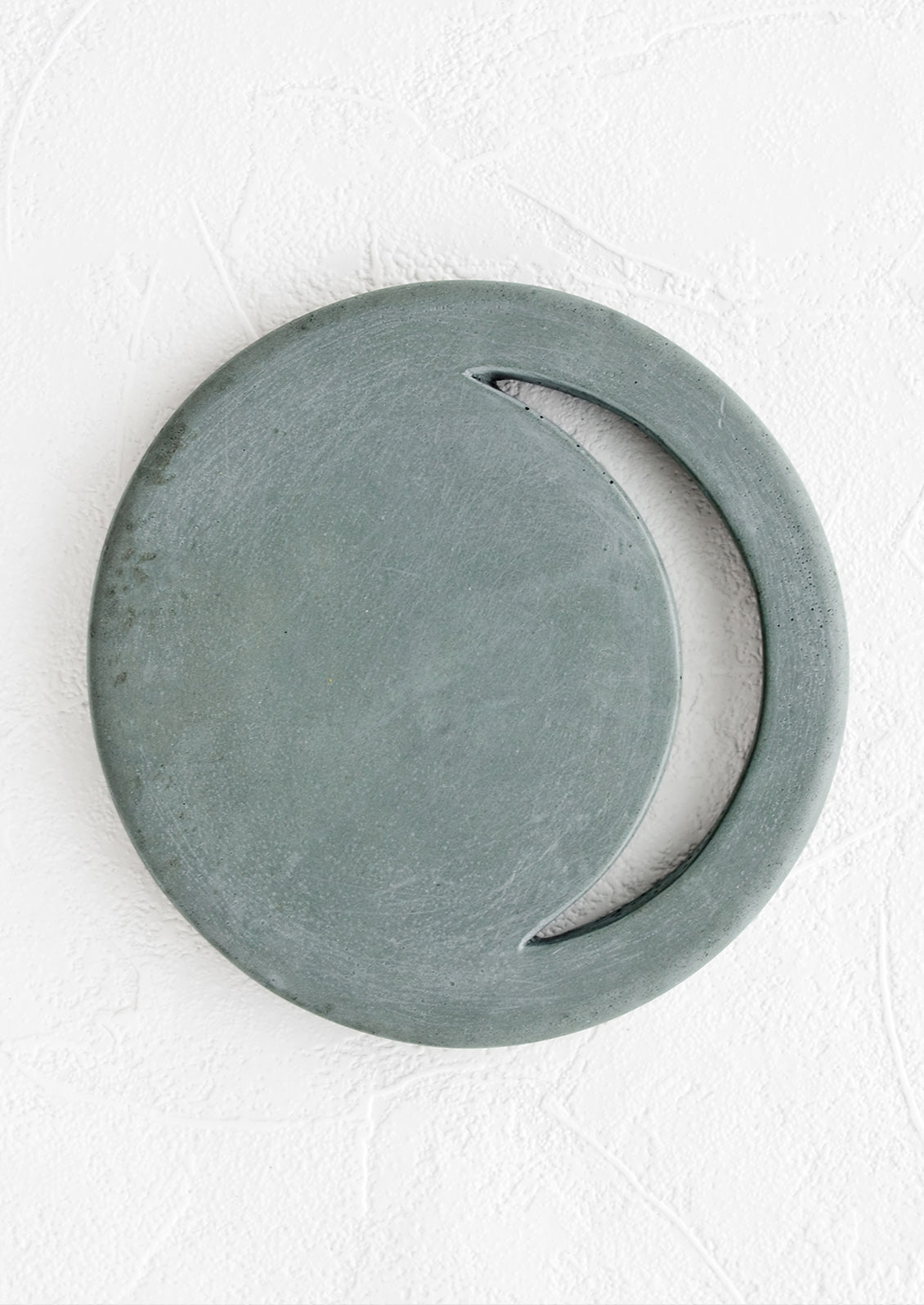 A round concrete trivet in marine color with crescent moon shaped cutout.