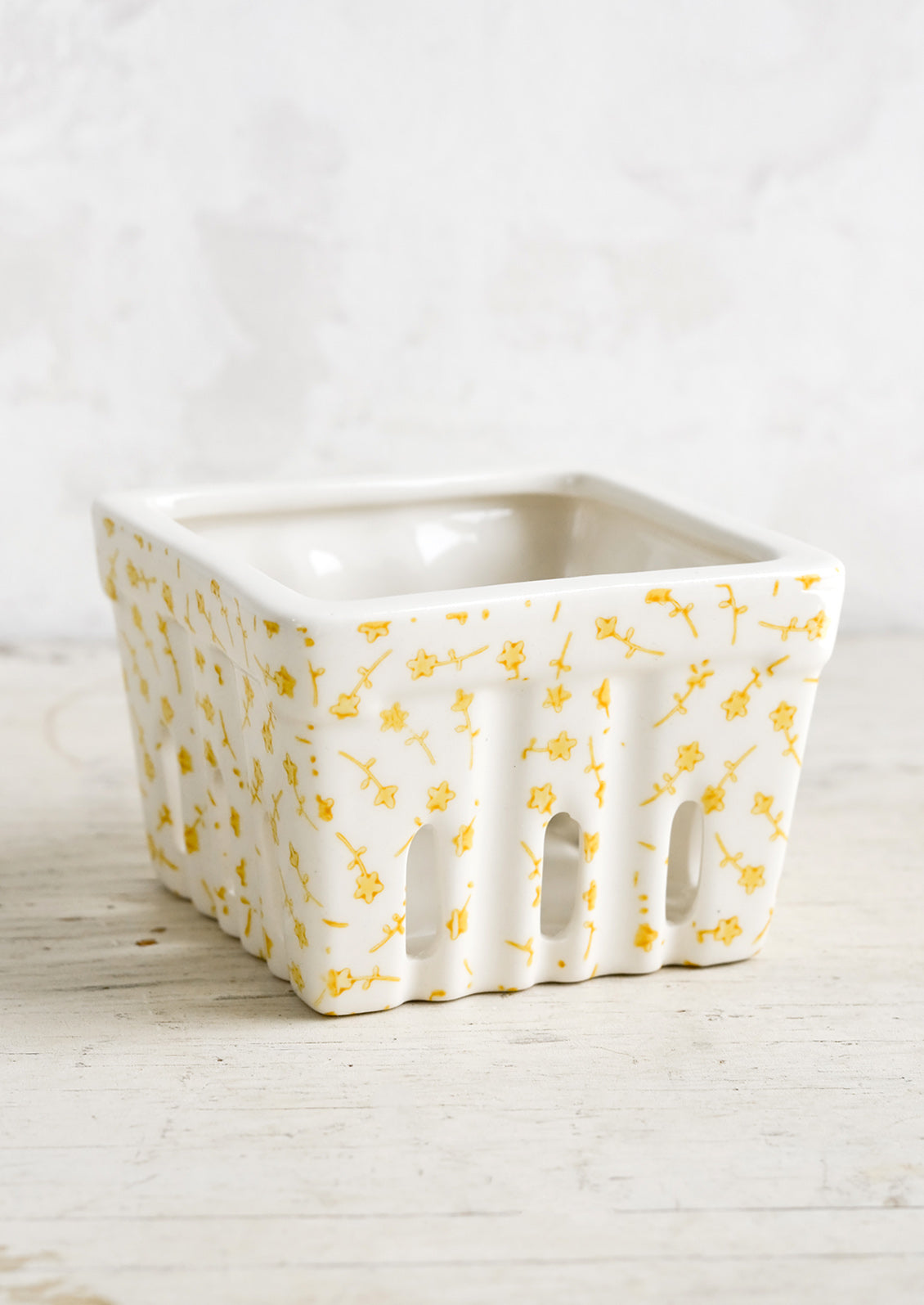 A ceramic berry basket  with yellow ditsy floral print on white ceramic.
