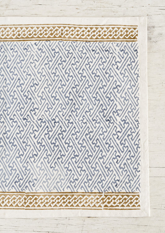 A cotton placemat with block print design, ochre borders at top and bottom with dusty blue maze patterned center.