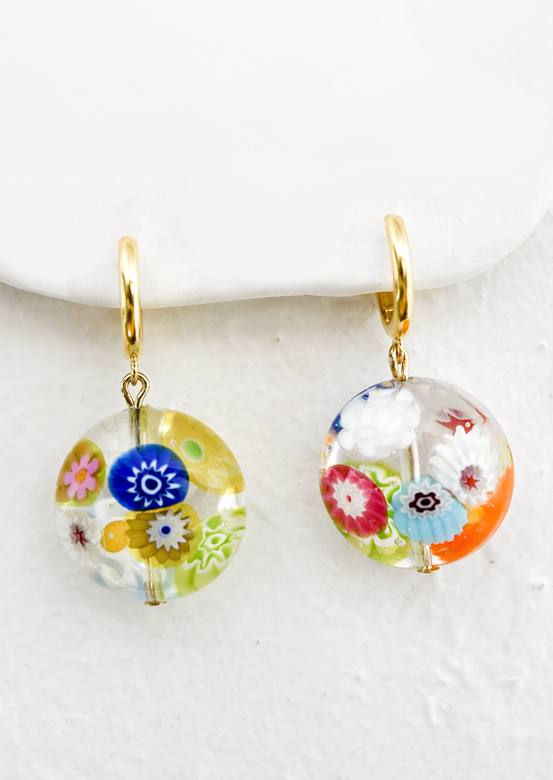 A pair of gold huggie hoops with multicolor murano glass beads.