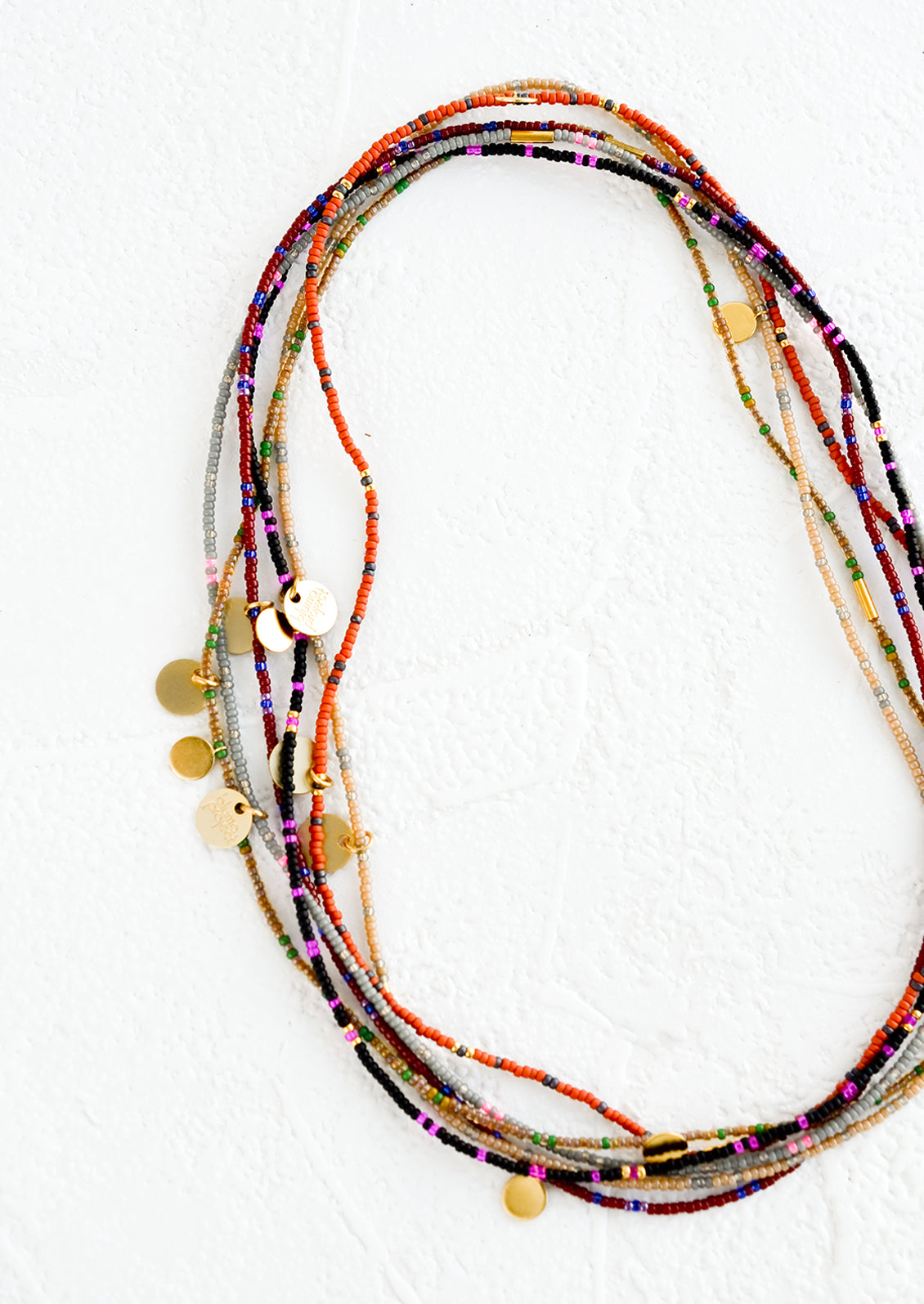 A layered, stacked pile of seed bead choker necklaces with brass charm details.