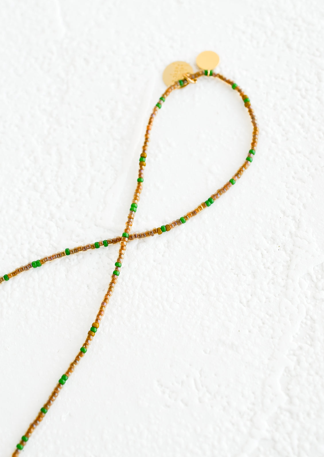 A strand of seed beads in coffee and green with brass charm details.