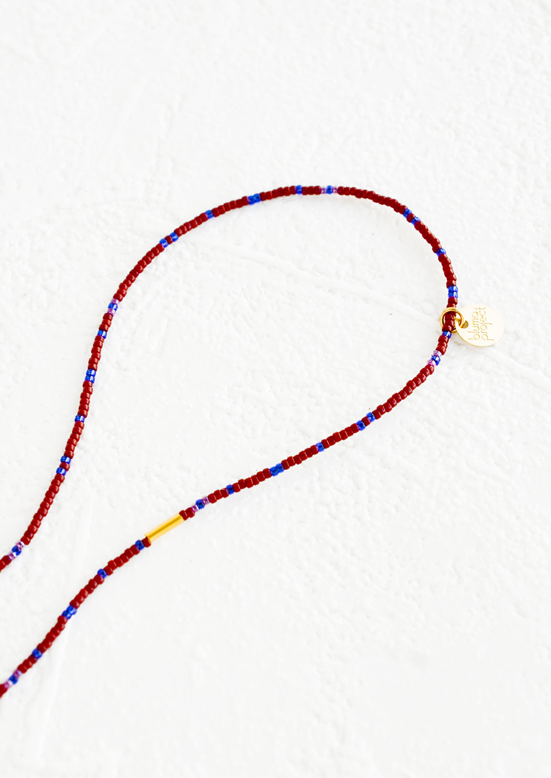 A strand of seed beads in burgundy and blue with brass charm details.