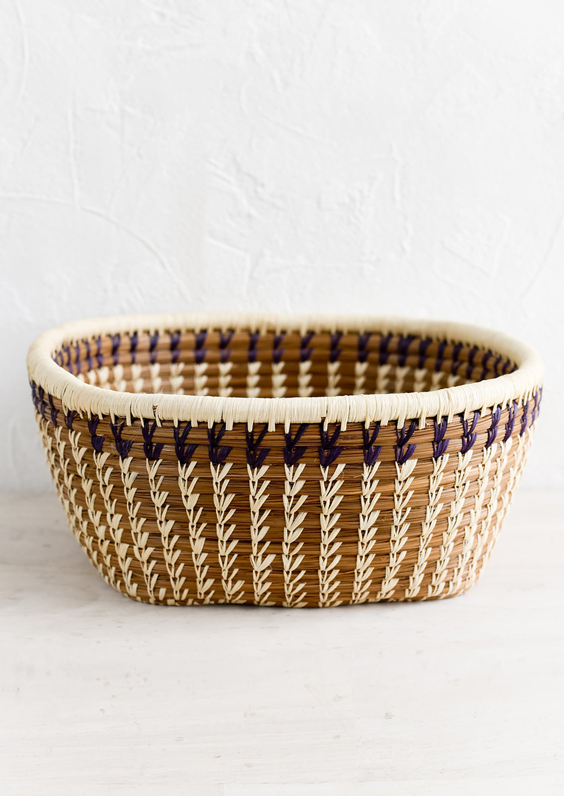 An open top woven storage basket in rounded square shape.