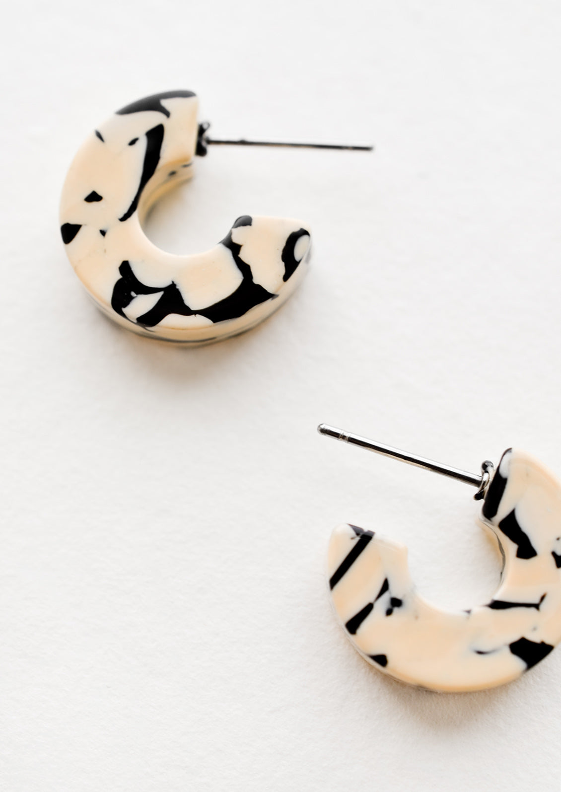 A pair of small acetate hoop earrings in tan and black marble.
