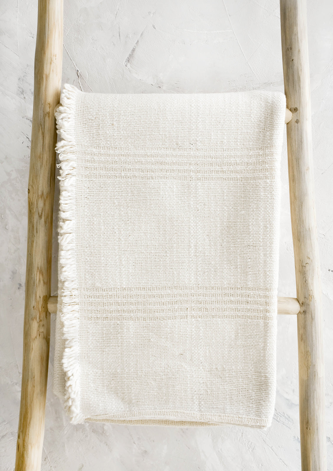 Woven throw made from natural undyed cotton with textural tonal stripes and fringed trim on one side