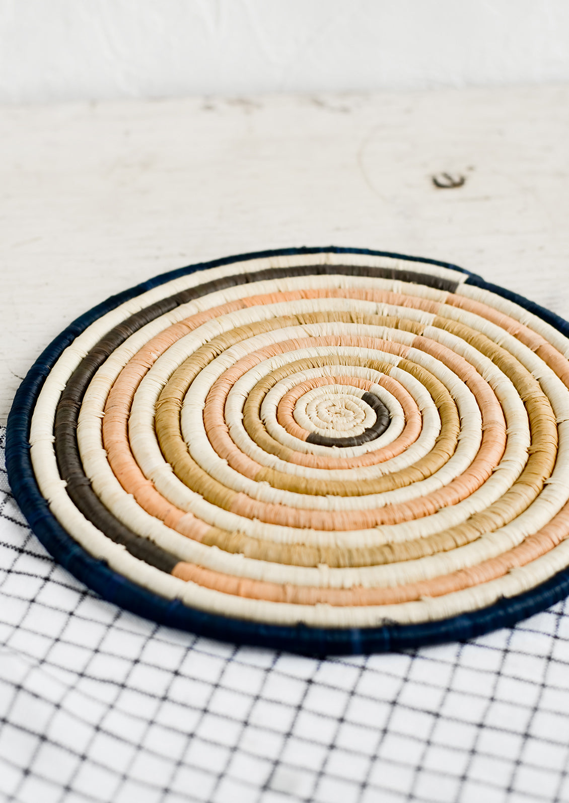 A round natural fiber trivet in peach and navy colorblock design.