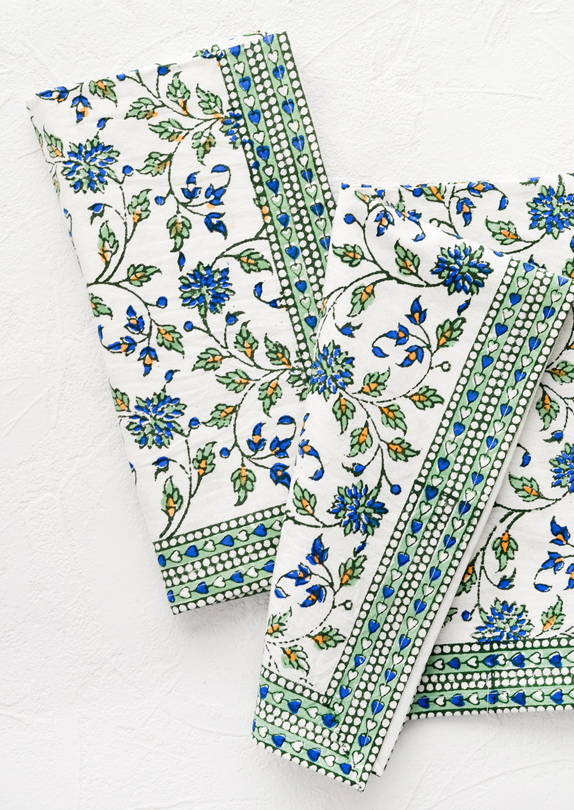 A pair of block printed floral napkins in green, blue and orange pattern with border.