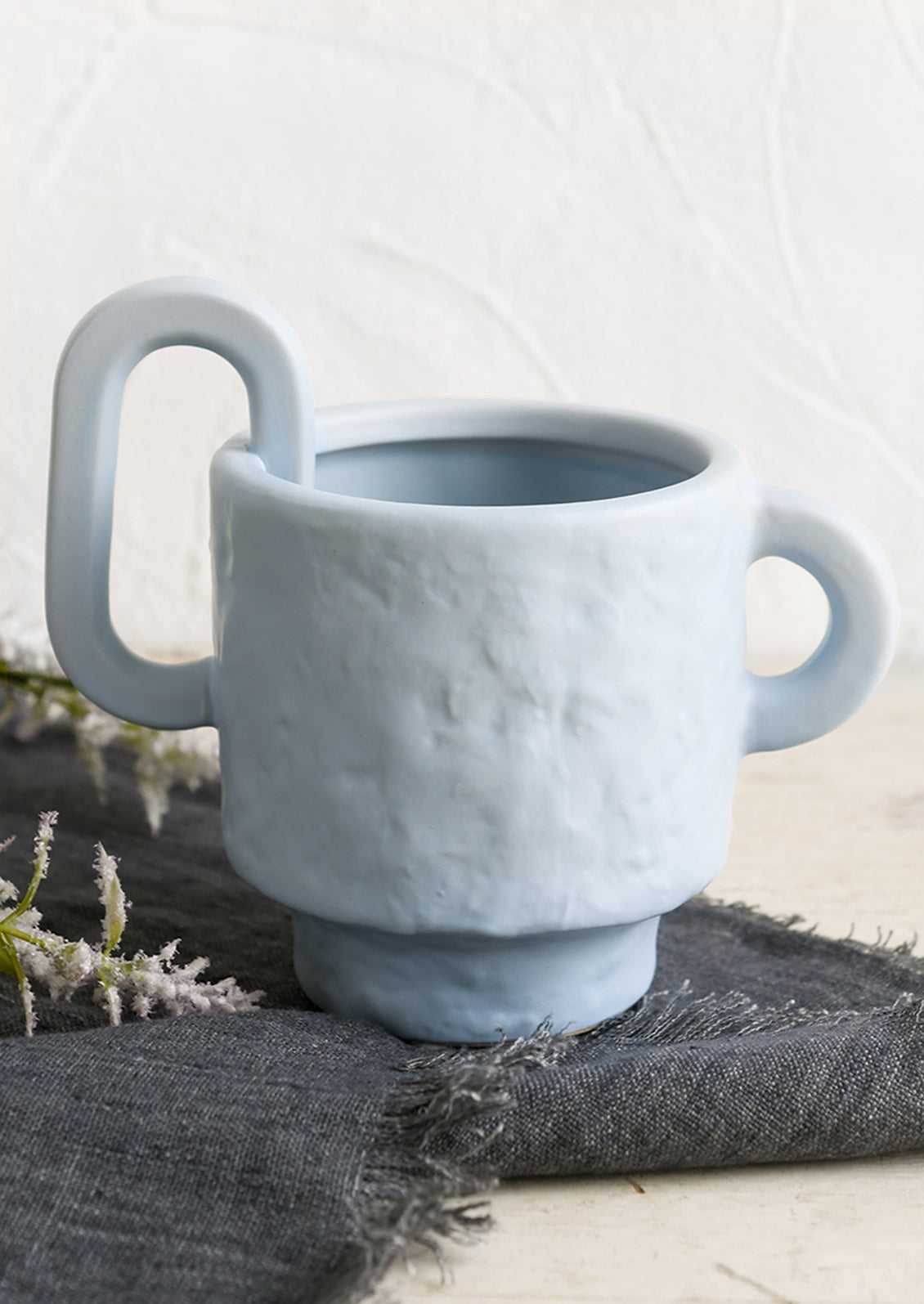 A sky blue planter with irregular texture and asymmetric handle detail.