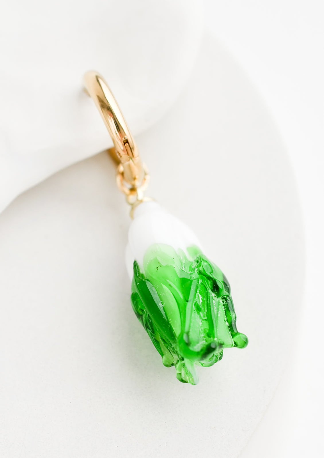 A single earring with glass cabbage charm on gold huggie hoop.