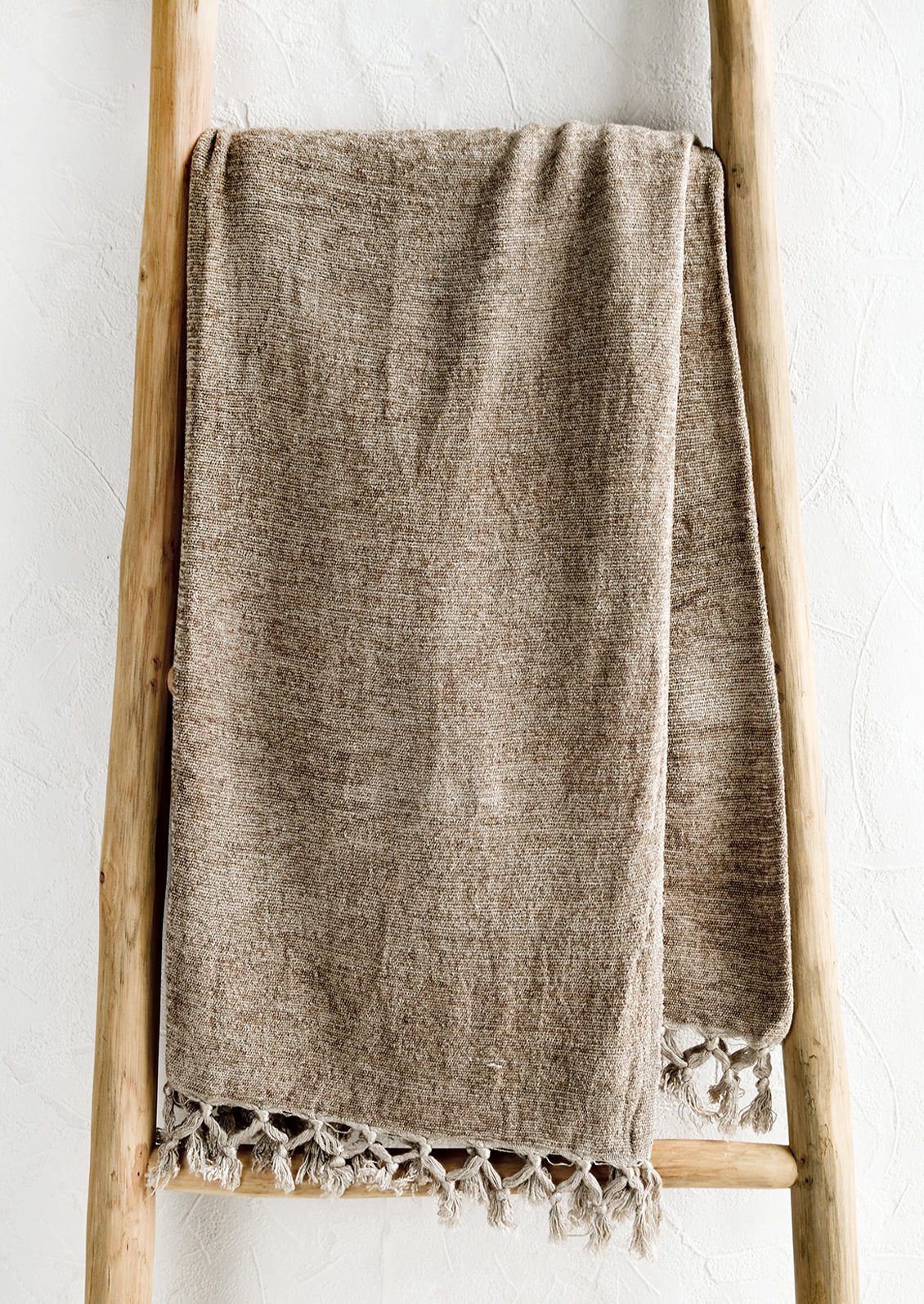 A chenille throw with knotted tassel trim in oat light brown color.