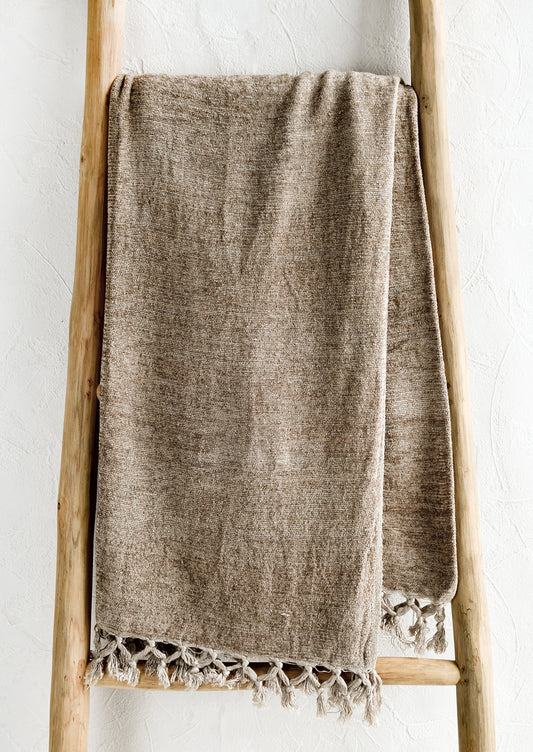 A chenille throw with knotted tassel trim in oat light brown color.
