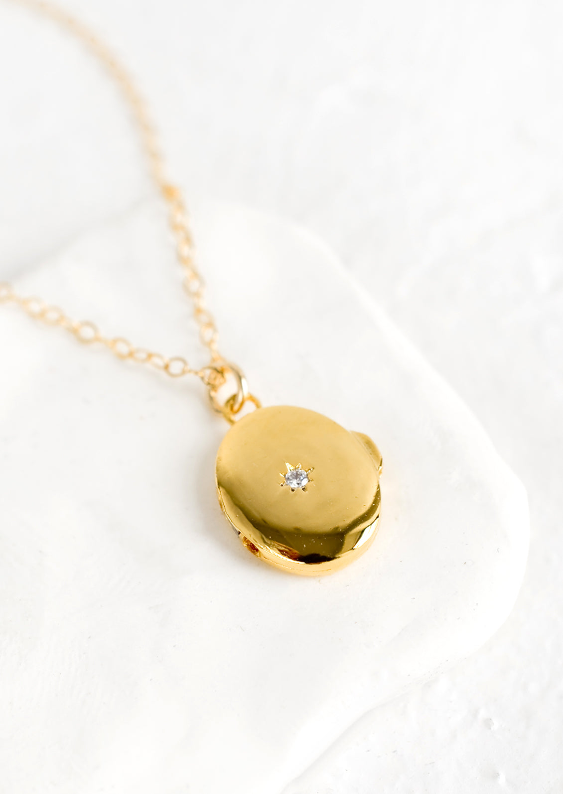 A gold locket necklace with north star crystal on front.