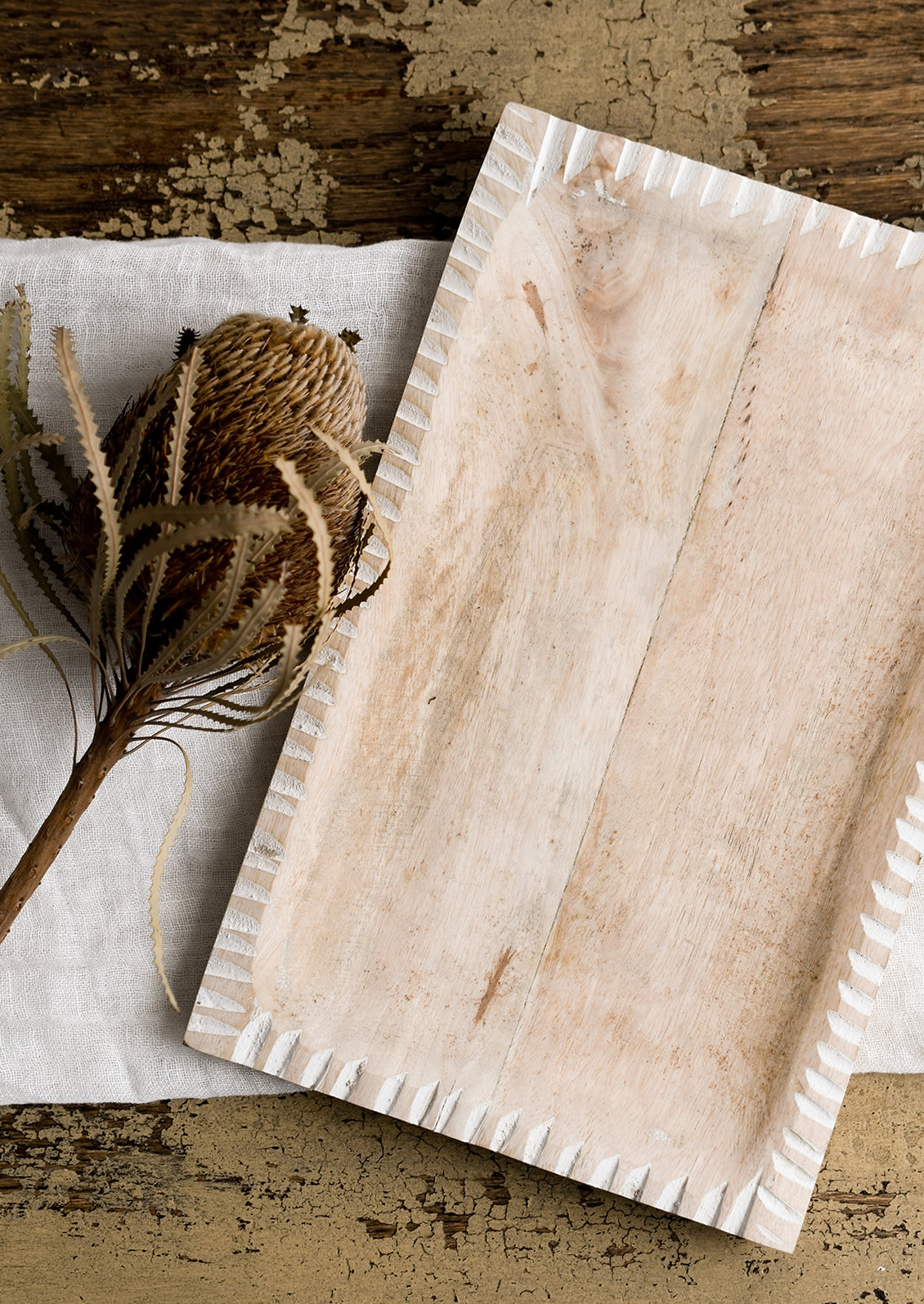 A dried protea flower displayed on a wooden tray.