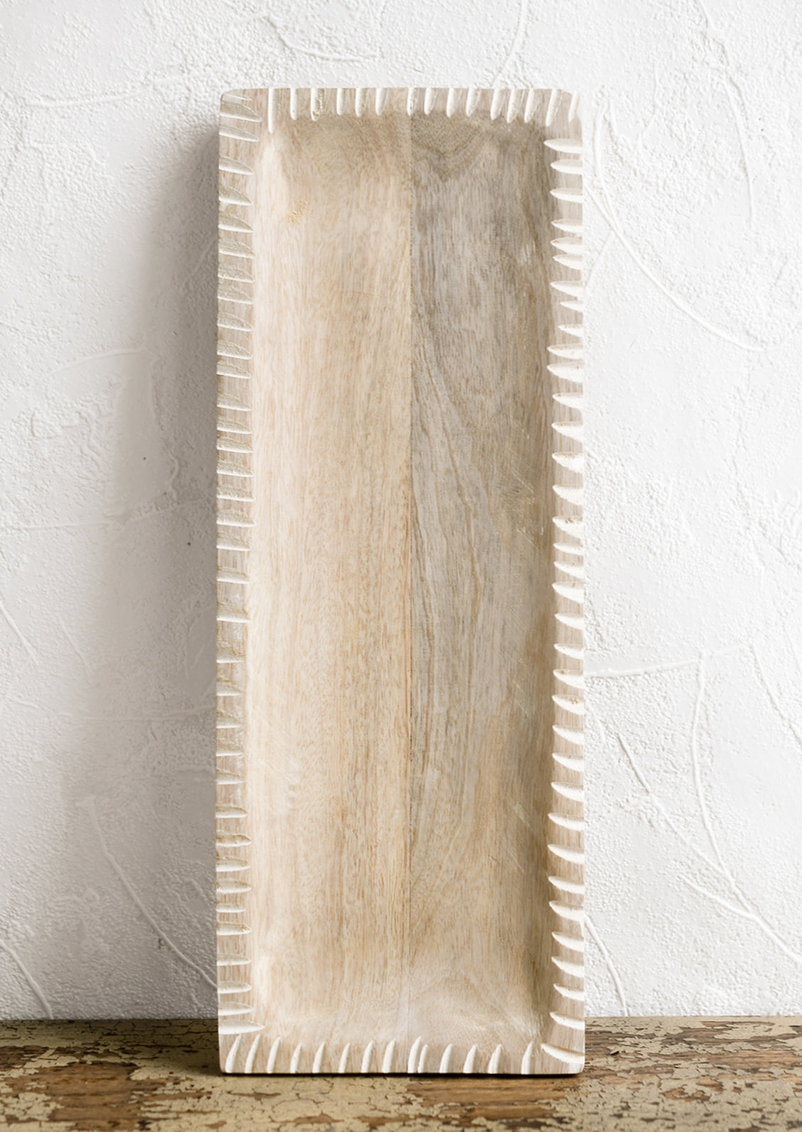A slim rectangular tray in light colored wood with white painted notched border.