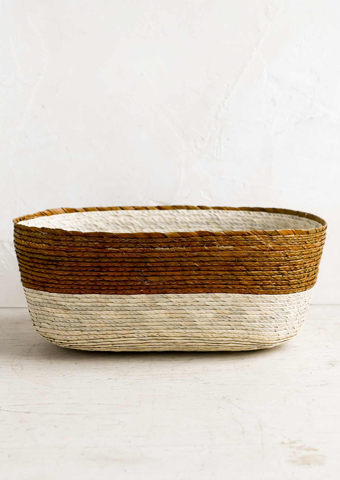 A two-tone oval shaped storage basket in natural and ochre.