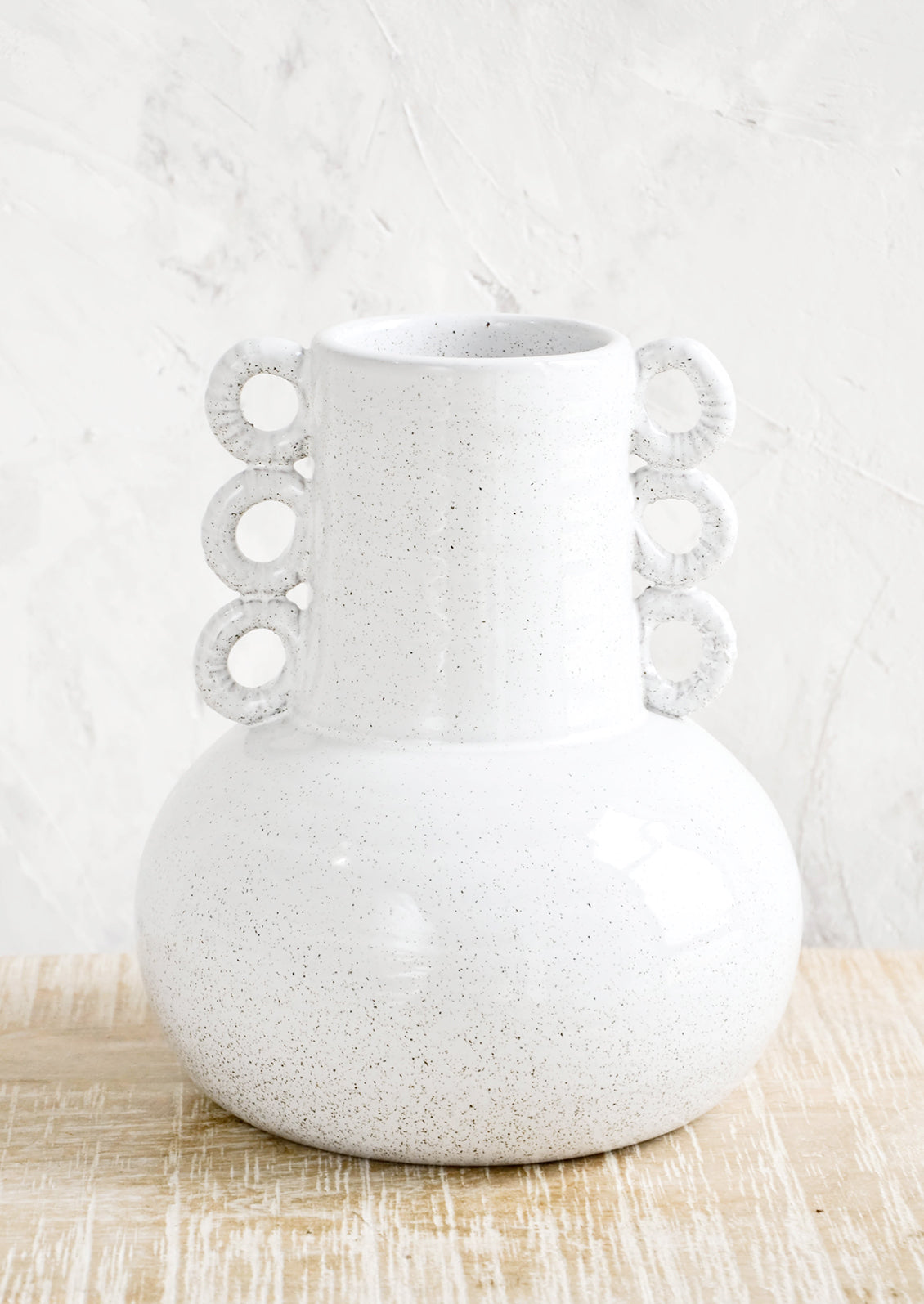 Ceramic vase in speckled white glaze. Shape is bulbous at bottom with tapered top and decorative round handles at sides.