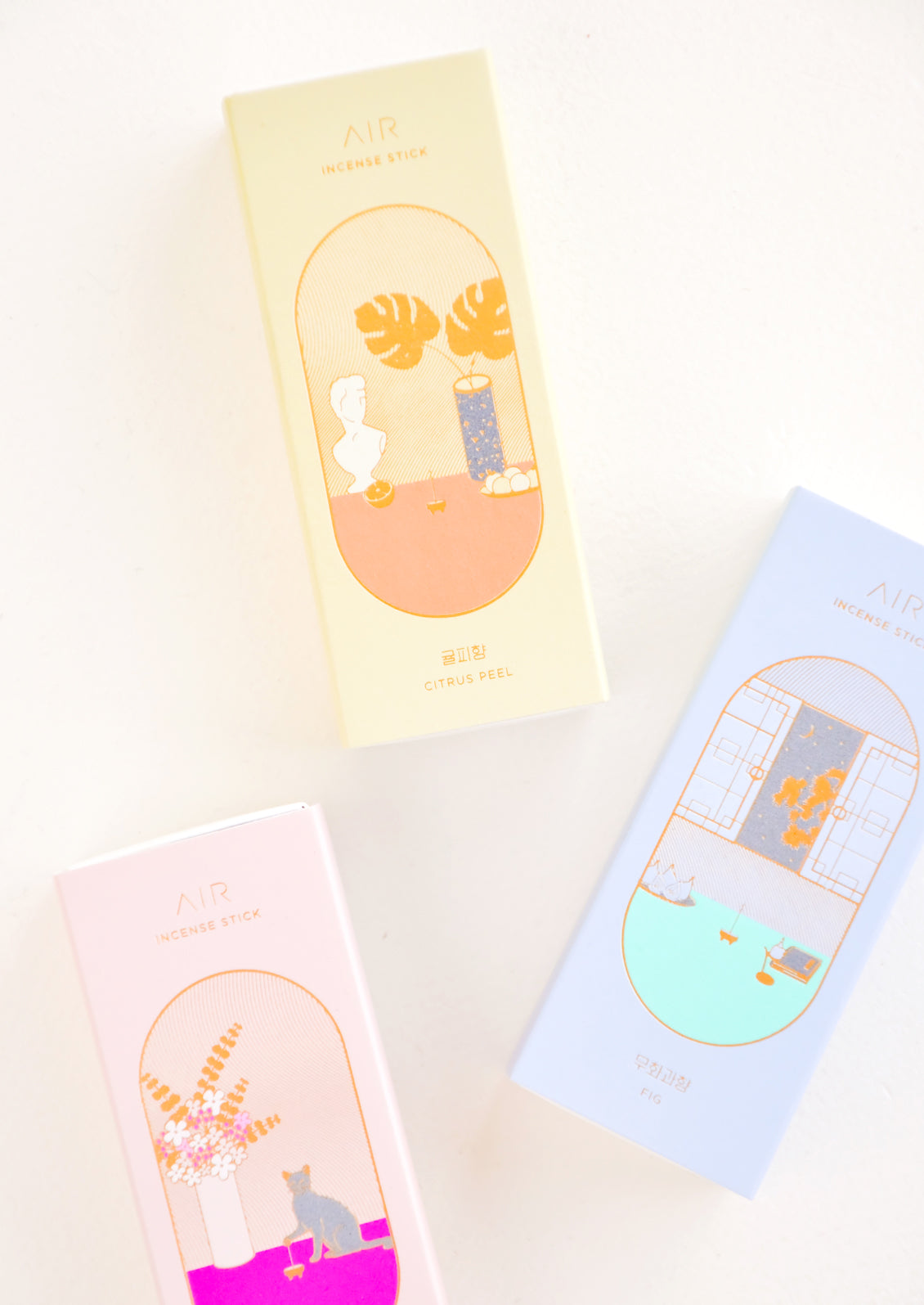 Three long boxes in pink, yellow, and blue with gold lettering