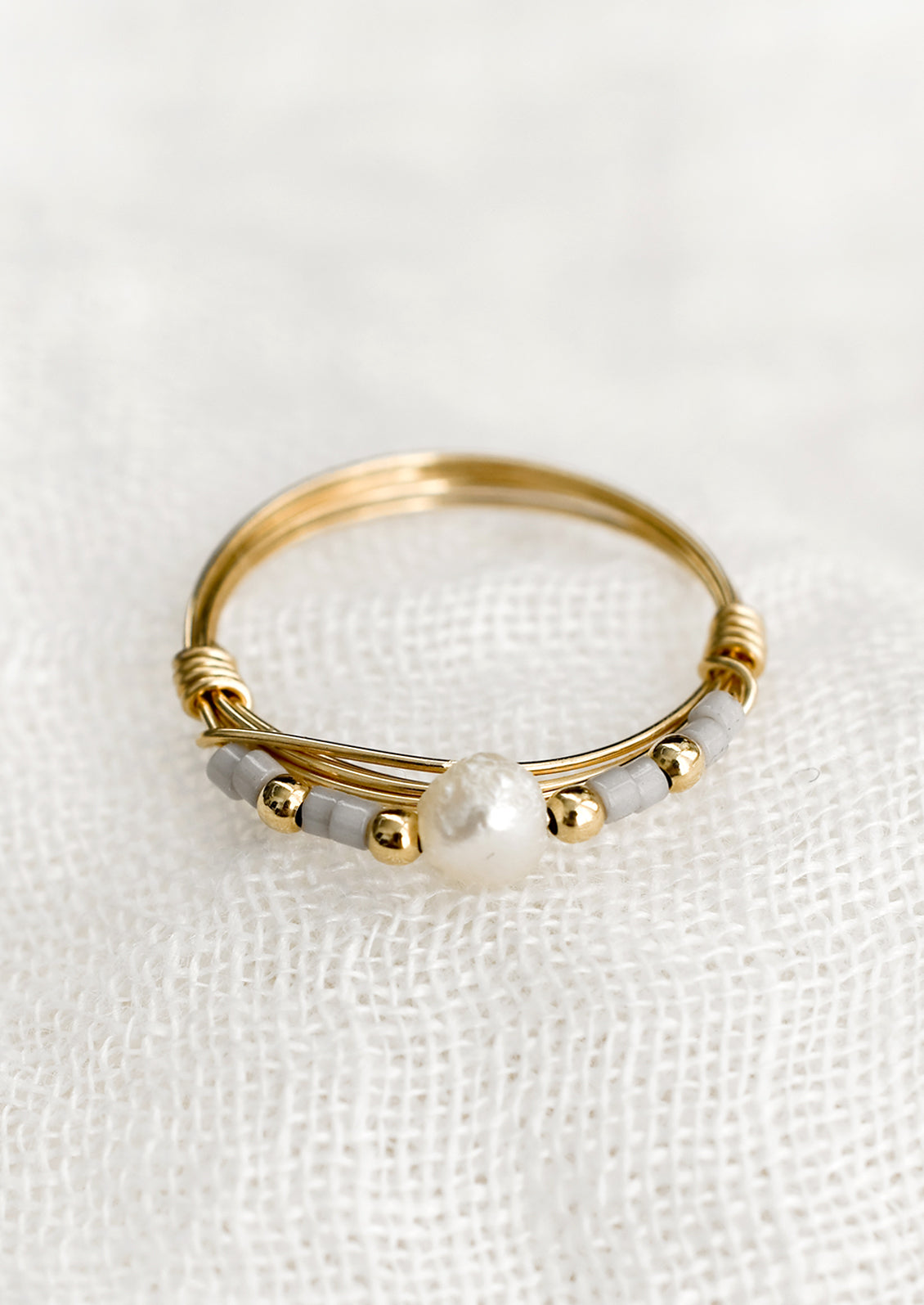 A gold wire ring with grey and pearl beads.