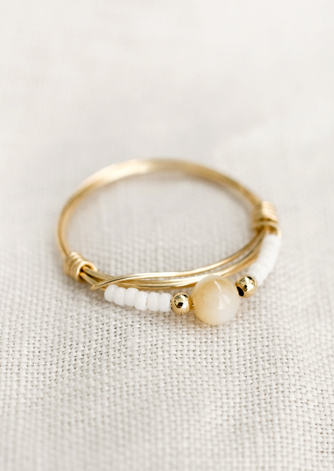 A gold wire ring with white and tan beads.