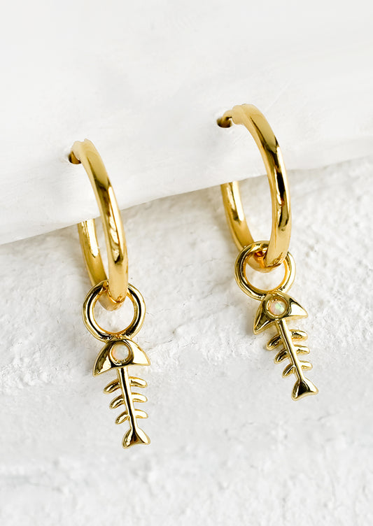 A pair of gold hoop earrings with fishbone charm and opal detailing.
