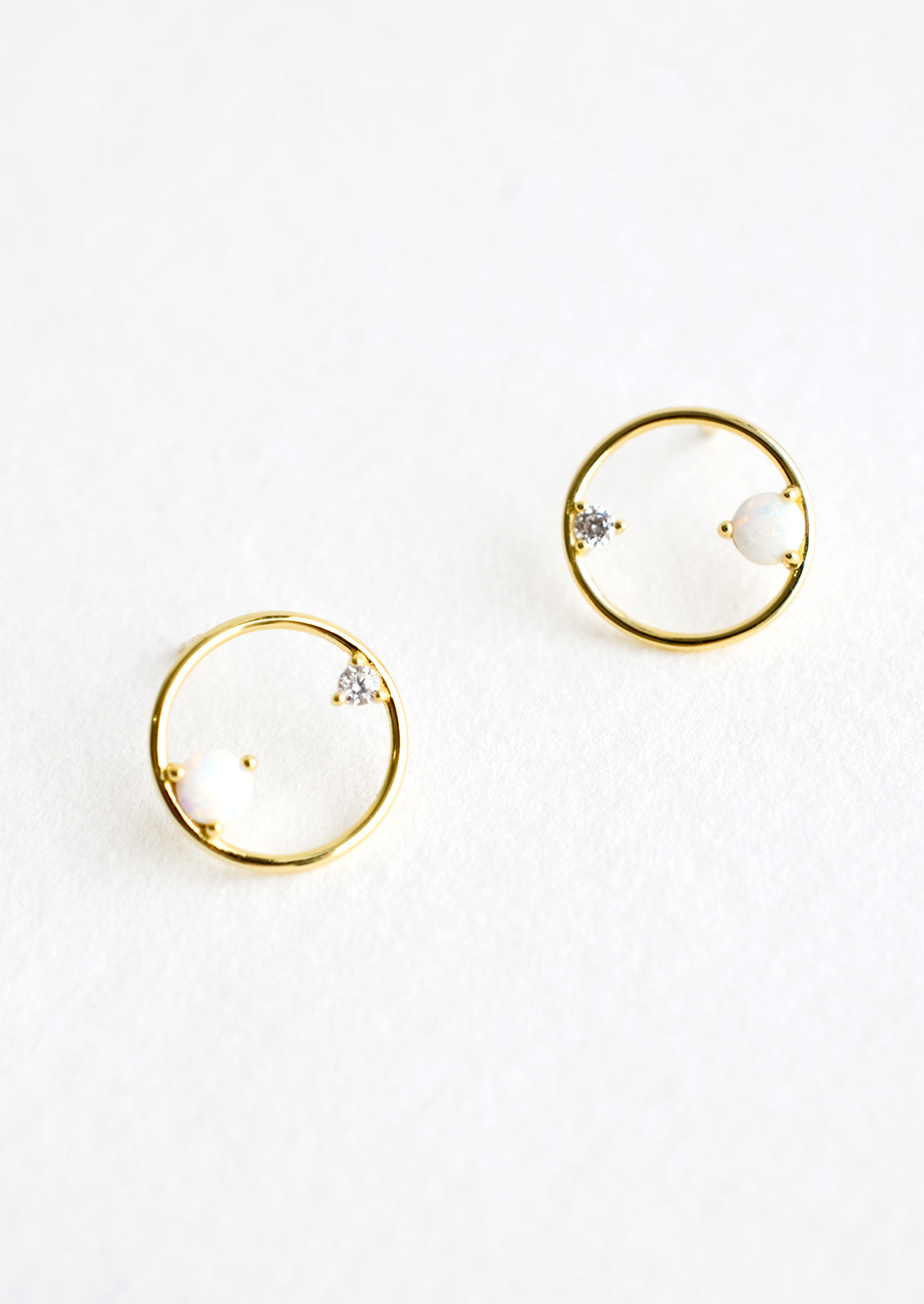 A pair of gold stud earrings in the shape of a circle with opal and crystal detailing.