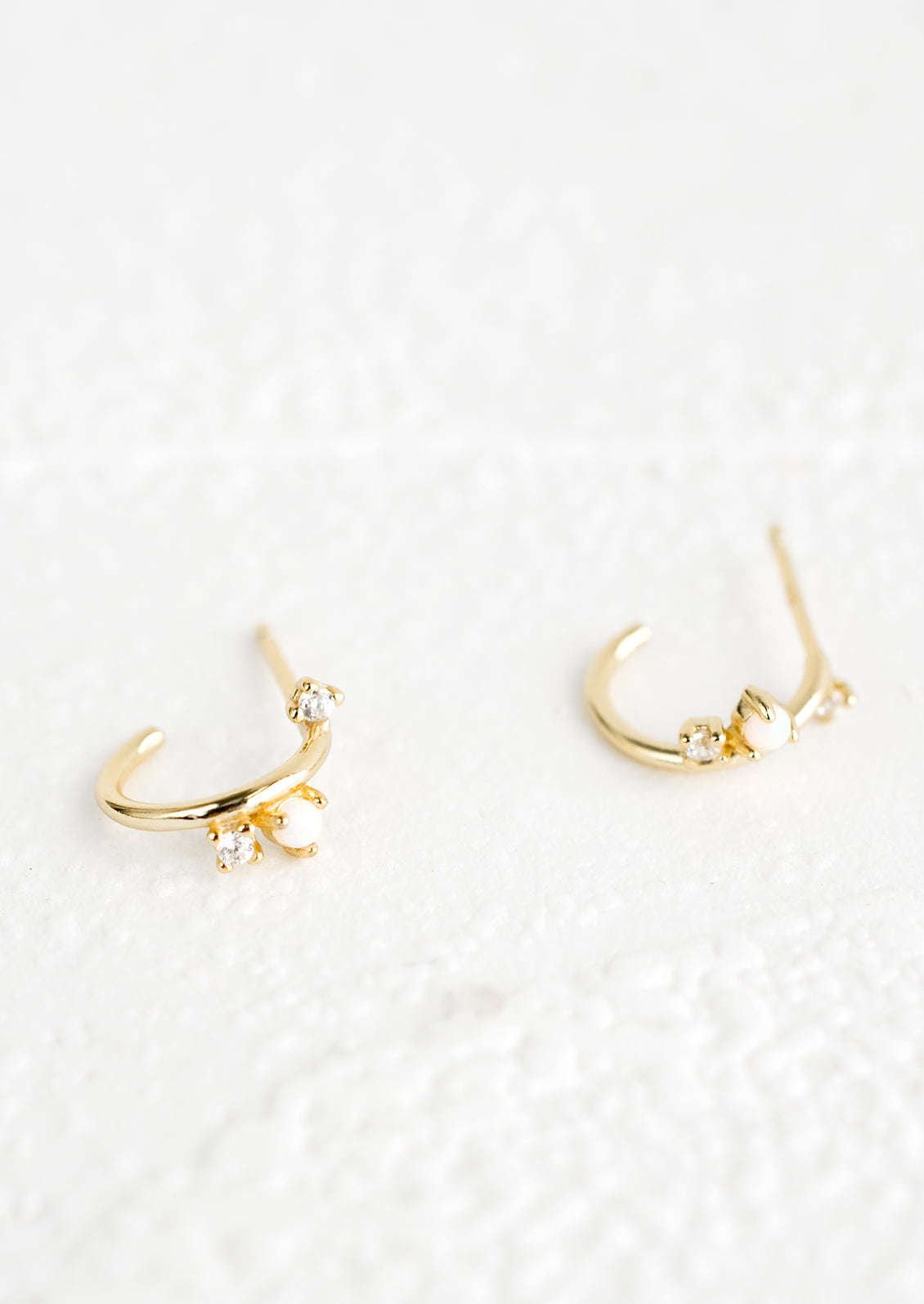 A pair of gold huggie hoop earrings with post back and opal and crystal accents