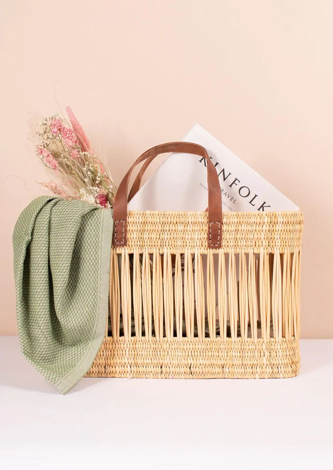 A tote-shaped woven reed basket with open air design, brown leather handles.