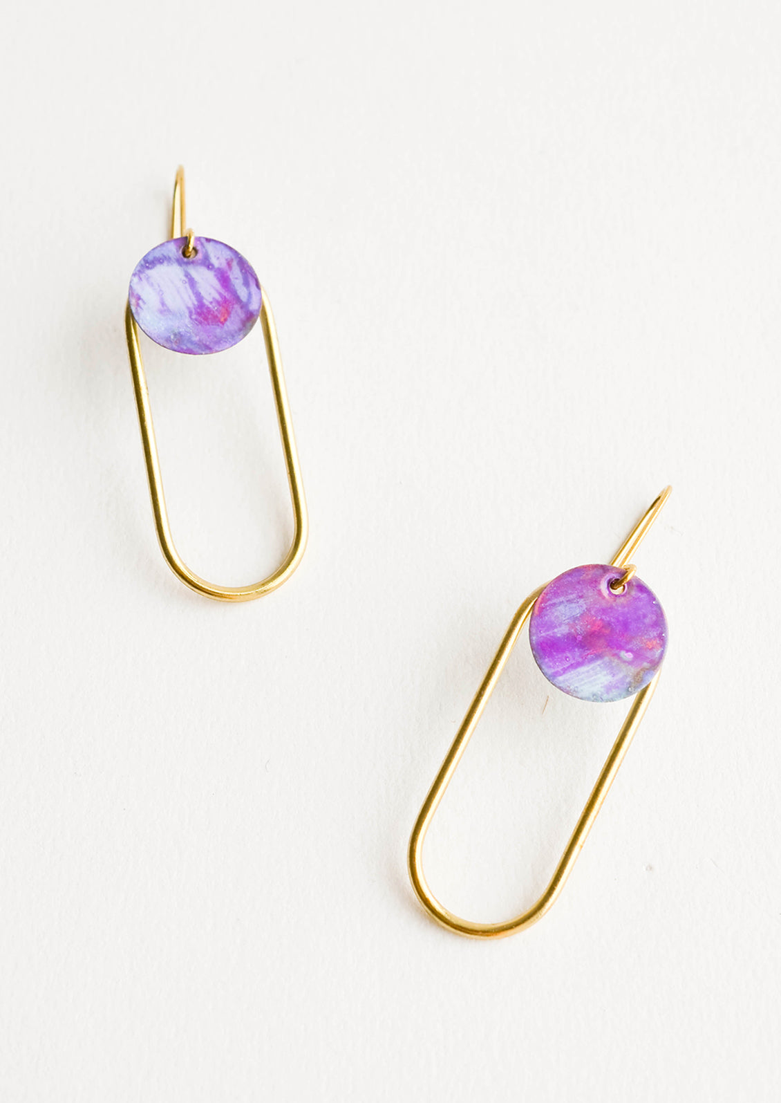 Pair of earrings in the shape of a hollow brass oval with a painted purple dot at the top.