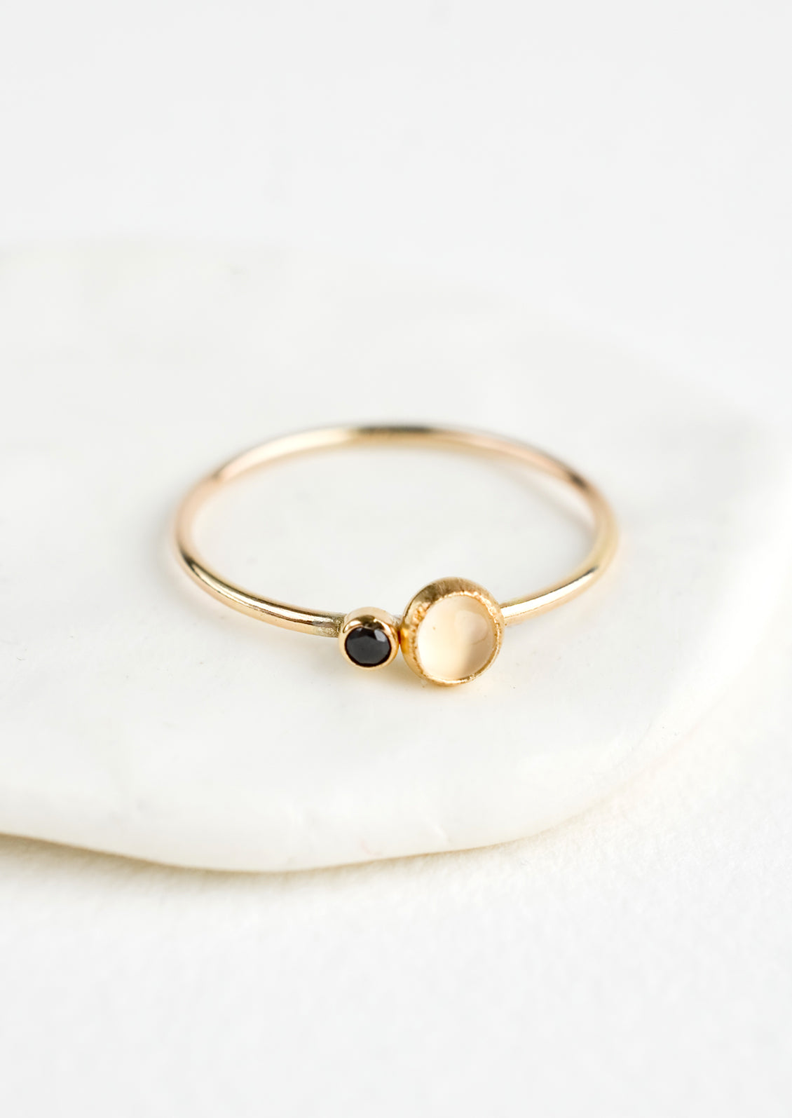 A gold ring with slim band and bezel set moonstone and black CZ.