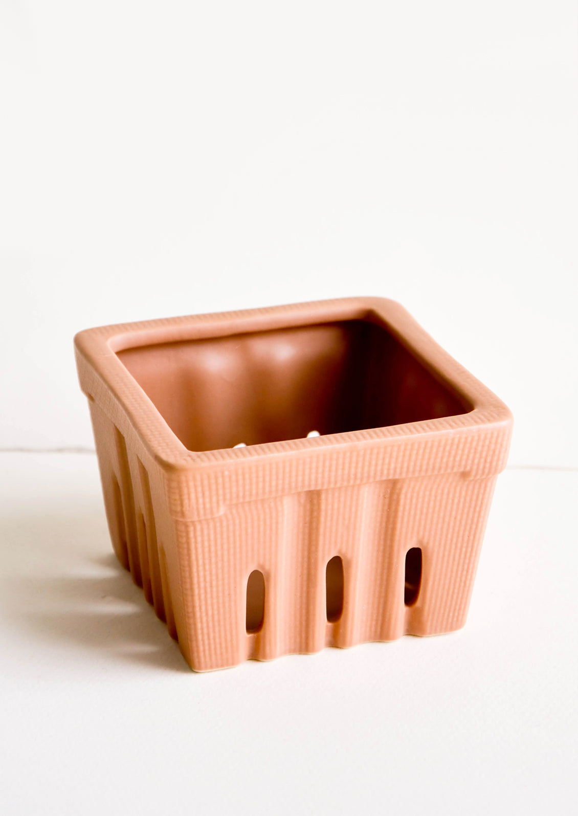 Ceramic basket in the style of disposable berry basket, shown in reddish brown